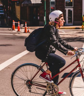 The Edge A woman riding a bicycle along a scenic path, wearing a helmet and enjoying the outdoors.